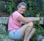 A woman sitting on the ground in front of some bushes.