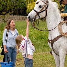 A woman and child petting the head of a white horse.